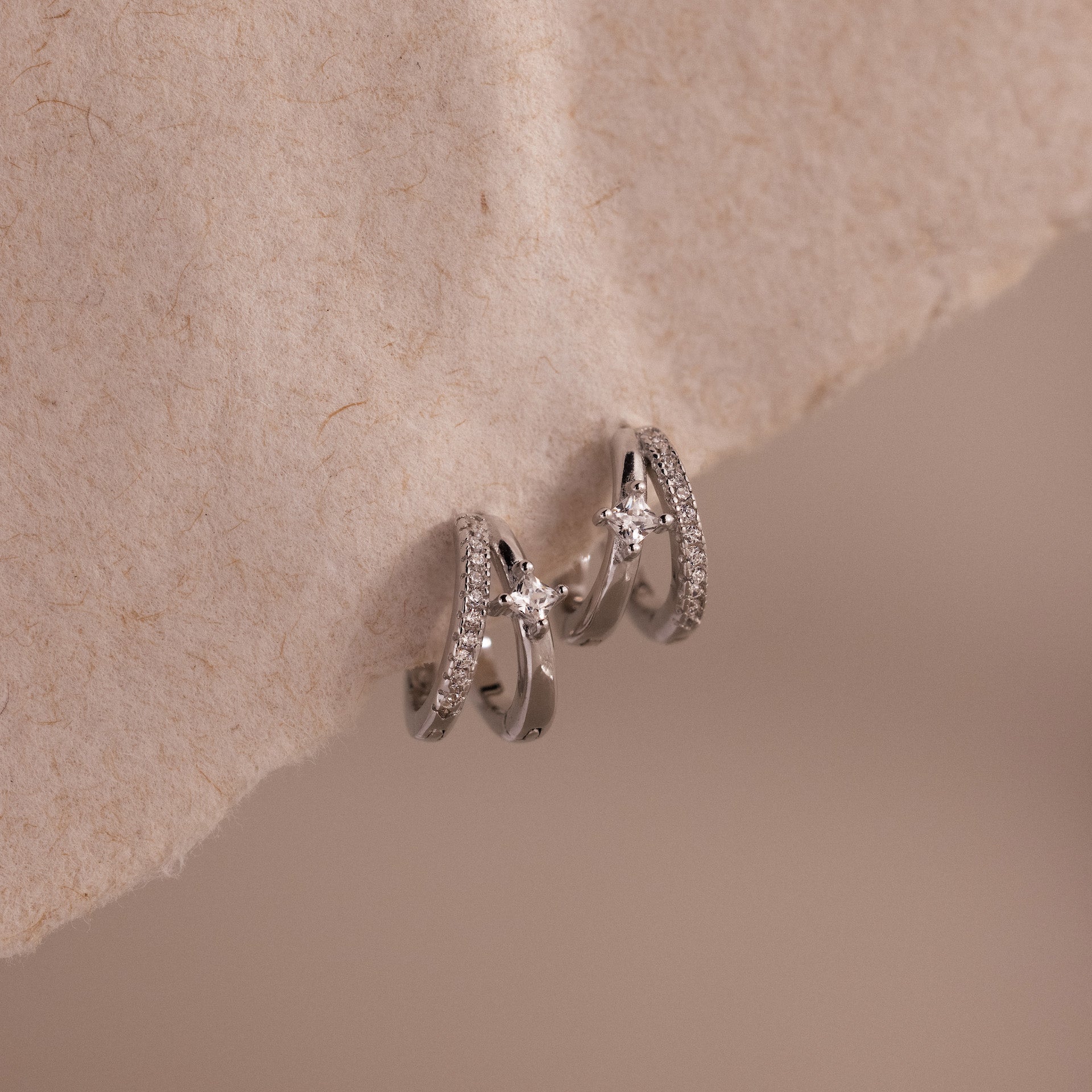 Pave Diamond Duo Huggies in Sterling Silver featuring pave-set stones and small star accents, displayed on a textured beige surface.