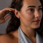 Woman with wavy brown hair and silver earrings, wearing a light gray halter top, touches her ear adorned with Pave Diamond Duo Huggies in Sterling Silver.
