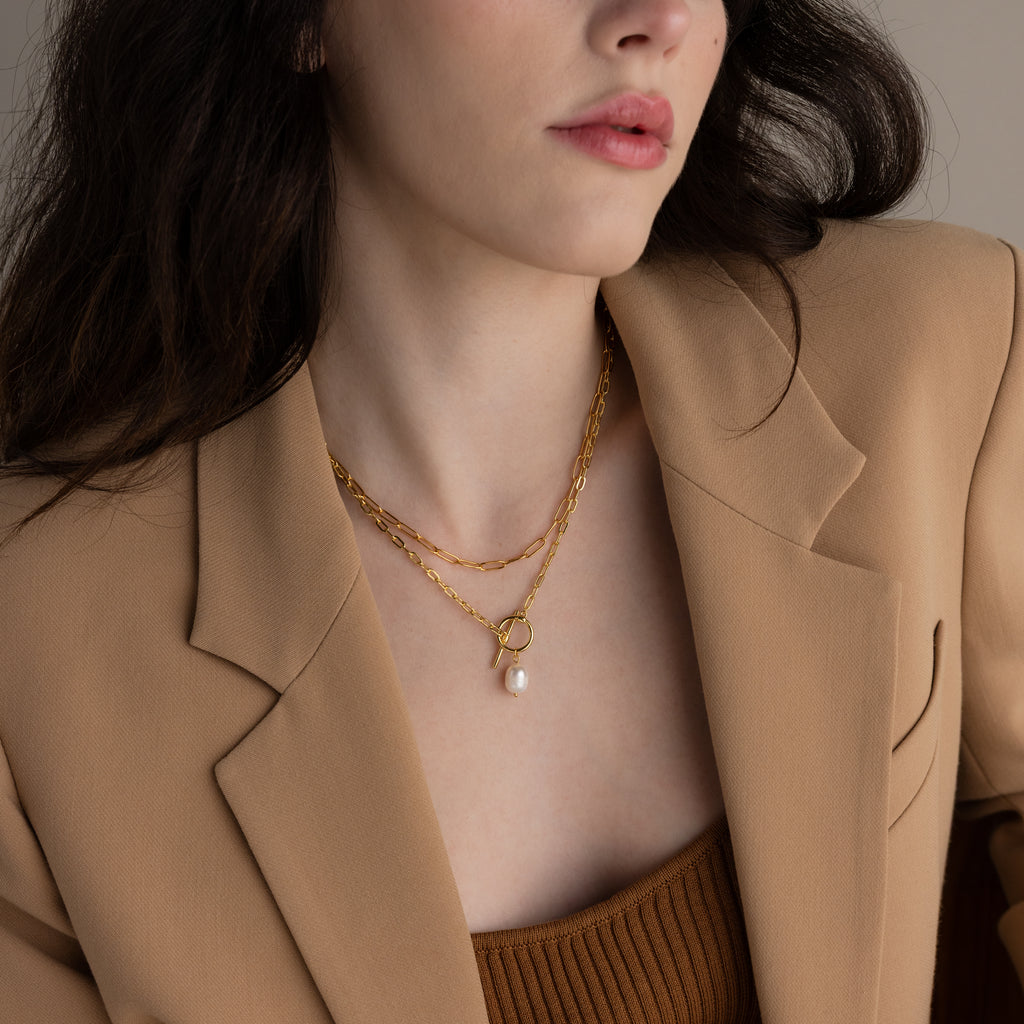 Woman in tan blazer and brown top wears minimalist jewelry, featuring a layered look with gold chains, a pearl pendant, and the Paperclip Chain Necklace.