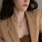 Woman in tan blazer and brown top wears minimalist jewelry, featuring a layered look with gold chains, a pearl pendant, and the Paperclip Chain Necklace.