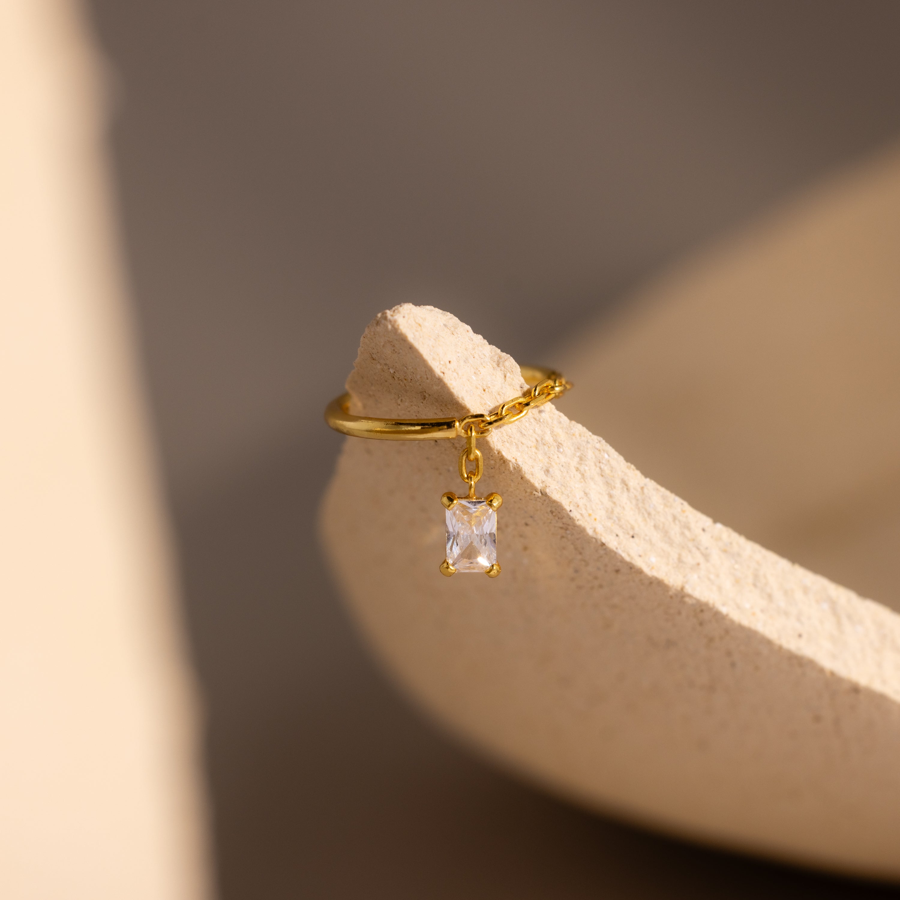 Opal Drop Chain Ring with a gold chain band and opal centerpiece, showcased on a textured beige surface under soft lighting.
