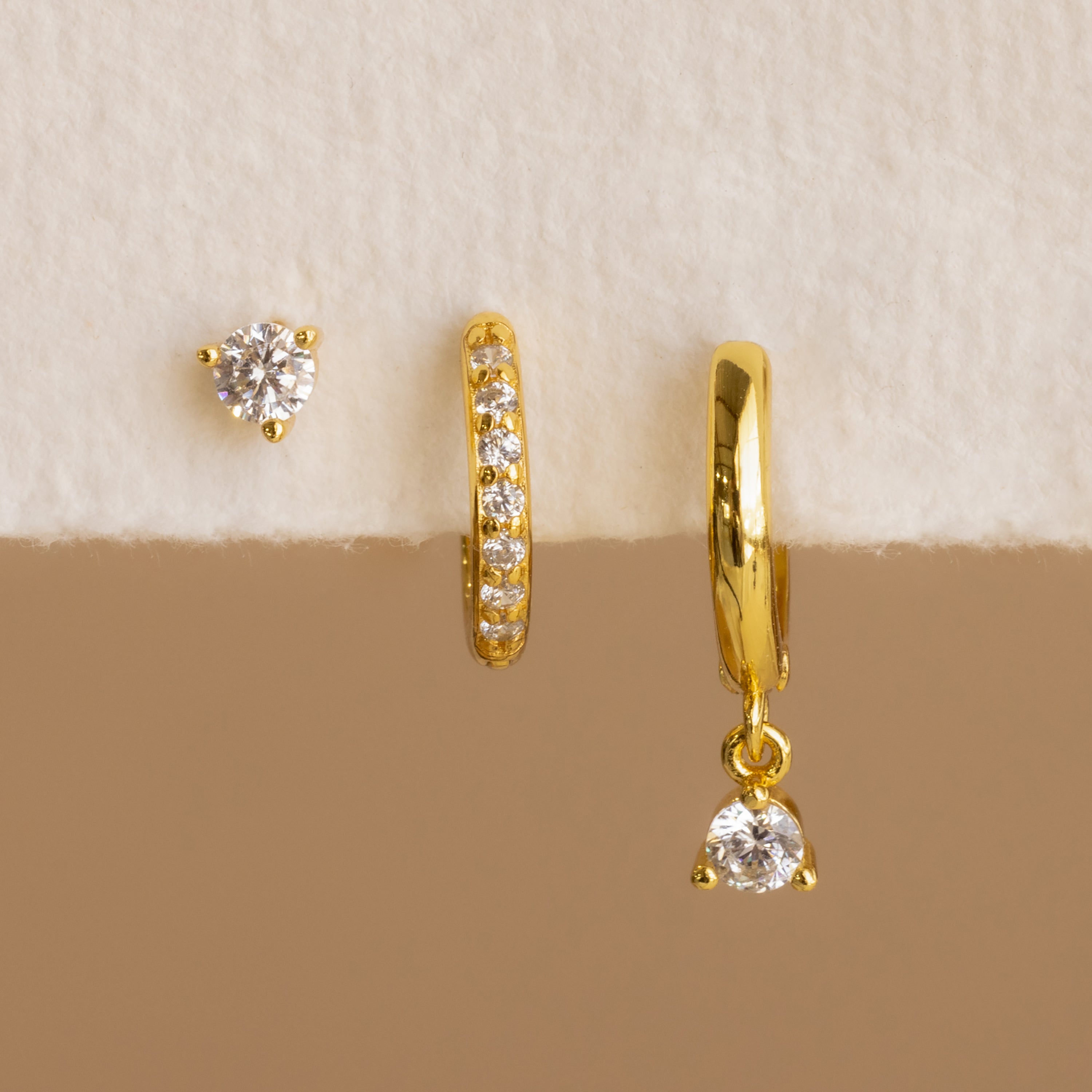 The Classic Diamond Earrings Set in 18K Gold features a stud, a diamond-studded hoop, and a hoop with a dangling diamond charm—ideal as timeless diamond earrings for any occasion or as sophisticated wedding earrings.