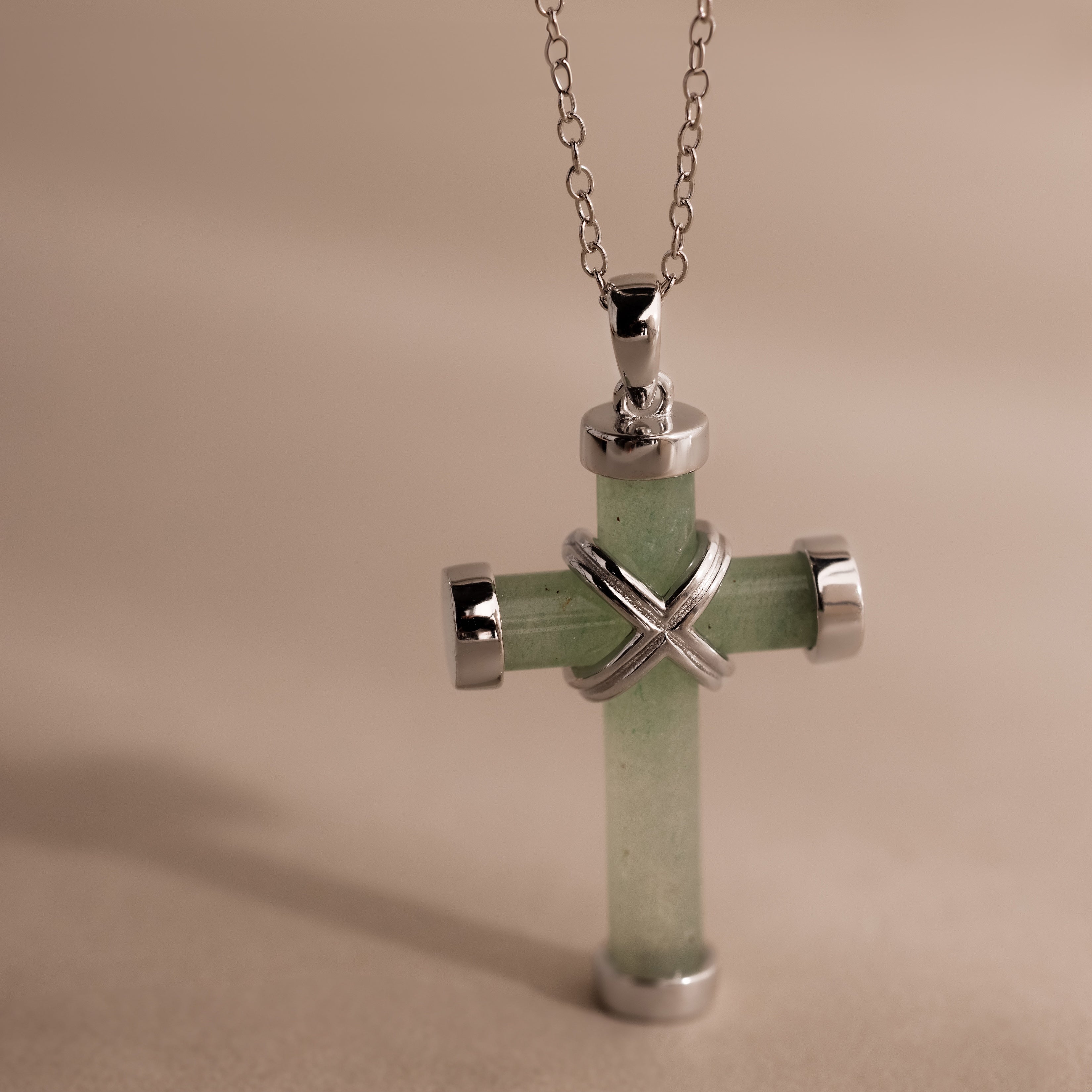 Silver chain necklace with a jade cross pendant, accented by polished gold end caps and an X shaped detail at the center.