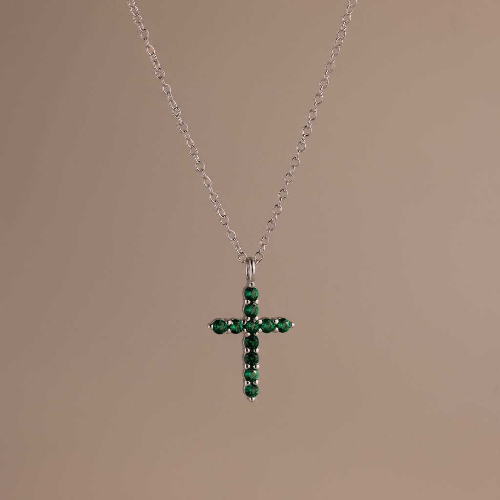 Silver chain necklace featuring a cross pendant set with small, round green stones against a neutral background.