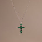 Silver chain necklace featuring a cross pendant set with small, round green stones against a neutral background.