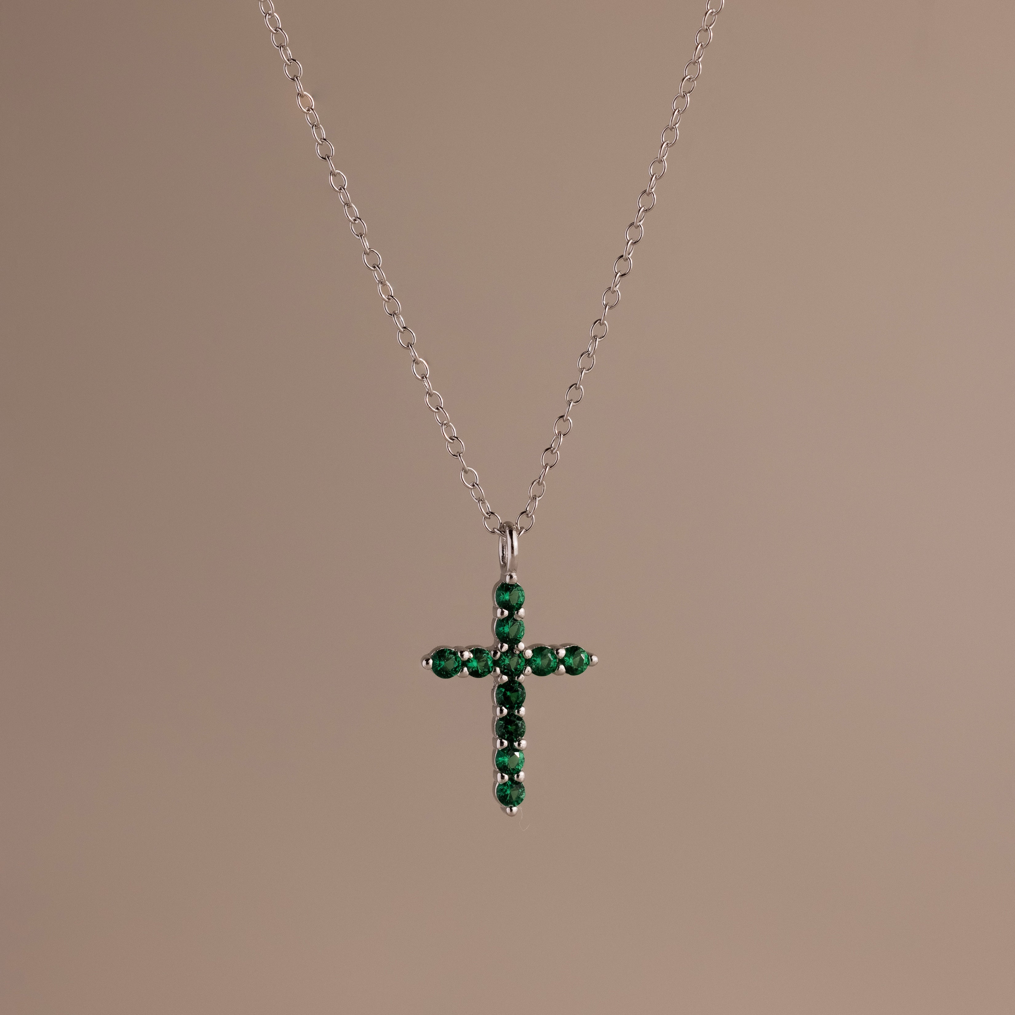 Silver chain necklace featuring a cross pendant set with small, round green stones against a neutral background.