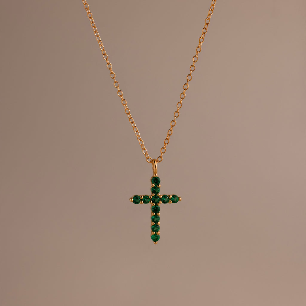 Gold chain necklace featuring a cross pendant set with small, round green stones against a neutral background.