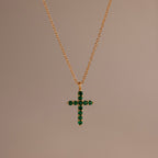 Gold chain necklace featuring a cross pendant set with small, round green stones against a neutral background.