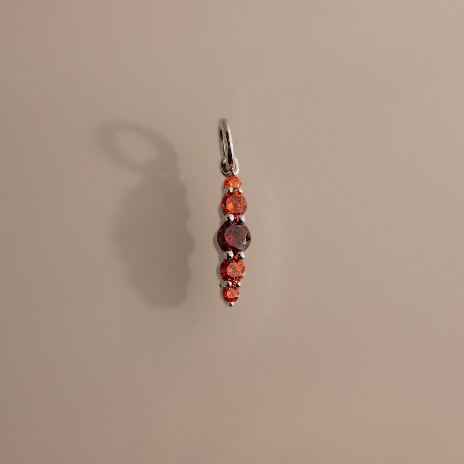 The Ombre Lace Garnet Charm is a silver pendant with five vertically arranged orange and red stones, making it a stunning birth month gift.