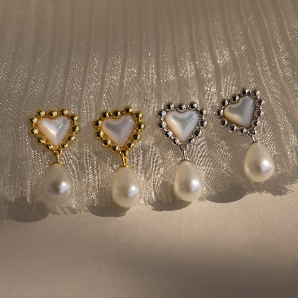 Four heart-shaped pearl beaded drop studs in 18K gold, beautifully displayed on pleated white fabric—perfect as Pearl Heart Earrings and a charming bridesmaid gift.
