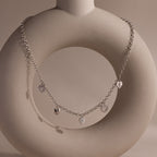 Silver heart charm necklace with five unique heart pendants displayed on a sculptural ceramic stand.