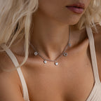 Model wearing a silver heart charm necklace featuring five unique heart pendants, styled with a neutral tank top.
