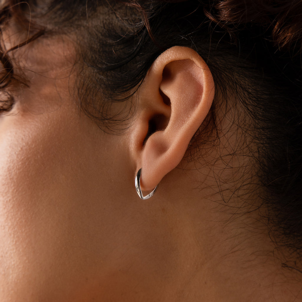 Close-up of a model wearing a small, sculptural leaf-shaped hoop earring in polished silver.