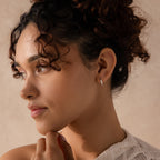 Model wearing a single sculptural leaf-shaped silver hoop earring on the left ear.