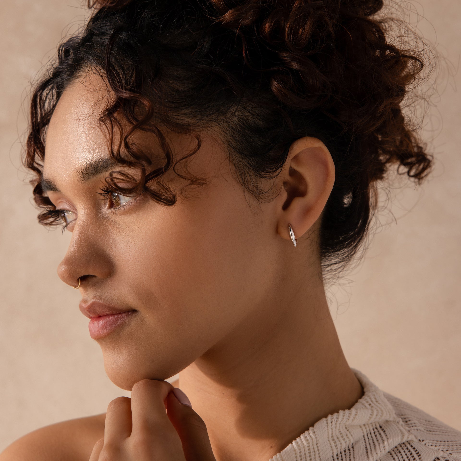 Model wearing a single sculptural leaf-shaped silver hoop earring on the left ear.