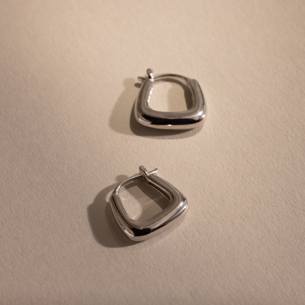 Pair of silver geometric hoop earrings displayed on a neutral background, highlighting their modern square shape and polished finish.