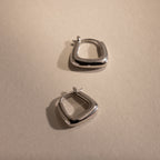 Pair of silver geometric hoop earrings displayed on a neutral background, highlighting their modern square shape and polished finish.