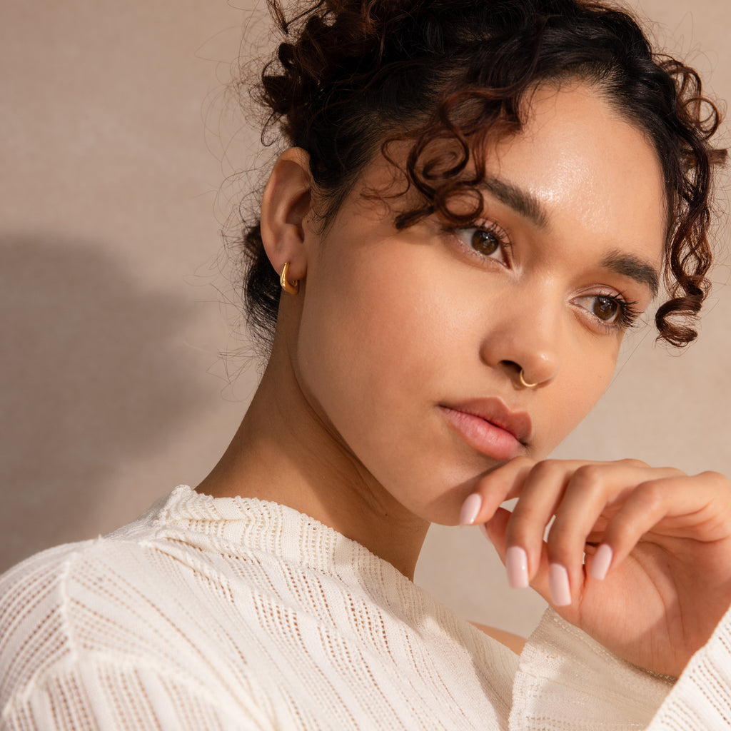 Model wearing small gold geometric square hoop earring styled with a neutral knit top.