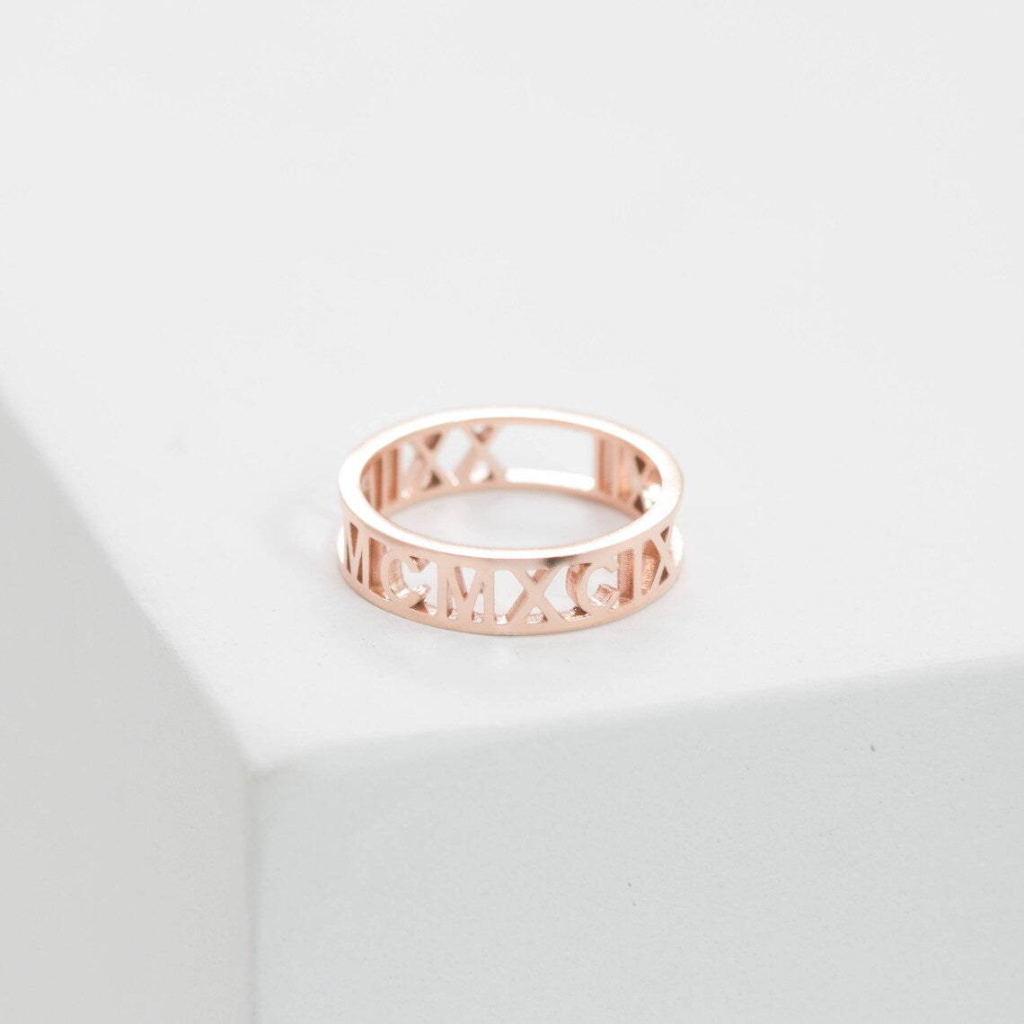 The Roman Numerals Ring in Rose Gold features elegant cut-out detailing, making it ideal for marking personal milestones or special dates. Shown on a white surface for a refined presentation.