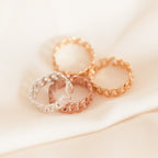 The Newsletter Curb Name Ring in Rose Gold, with its chic chain design, is displayed on a soft beige fabric background.