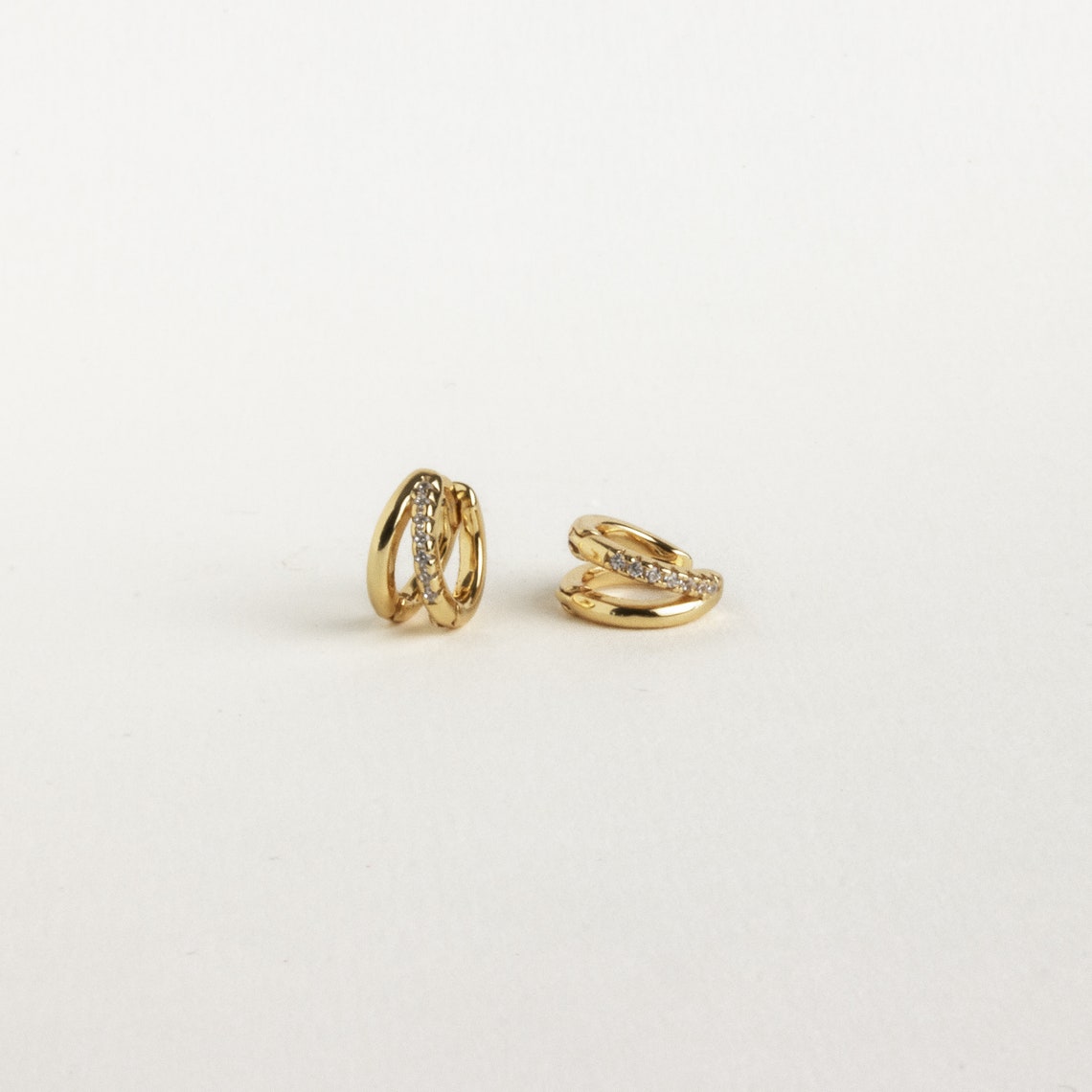 Two small gold Amelia Duo Huggies featuring embedded clear stones and pave accents, shown on a plain white background.