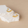 Gold cursive name earrings on a textured white surface with a beige background