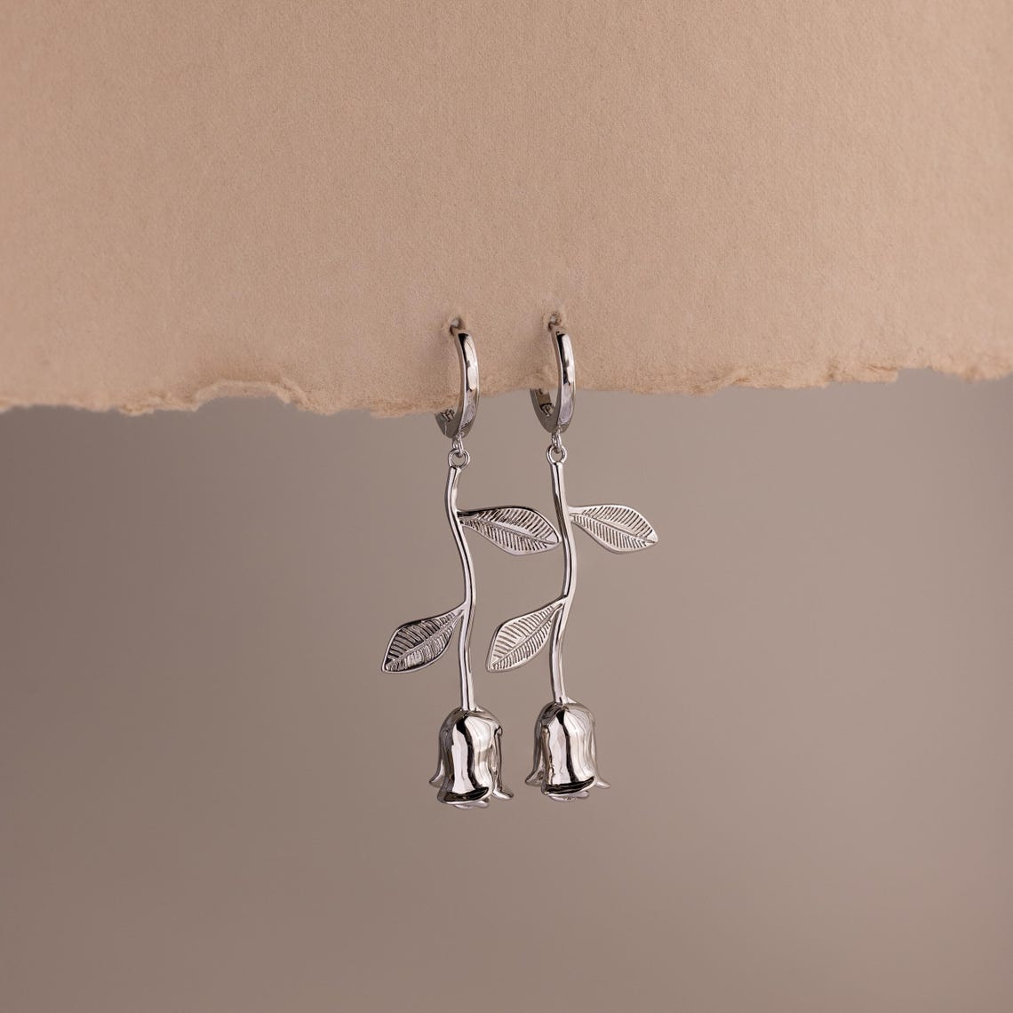 Dangling Silver earrings shaped like roses on a beige background