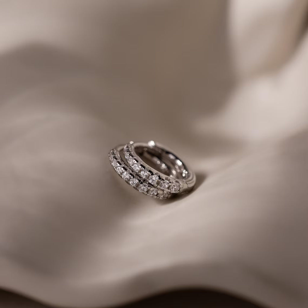 Silver hoop earrings with embedded diamond stones on a soft fabric background