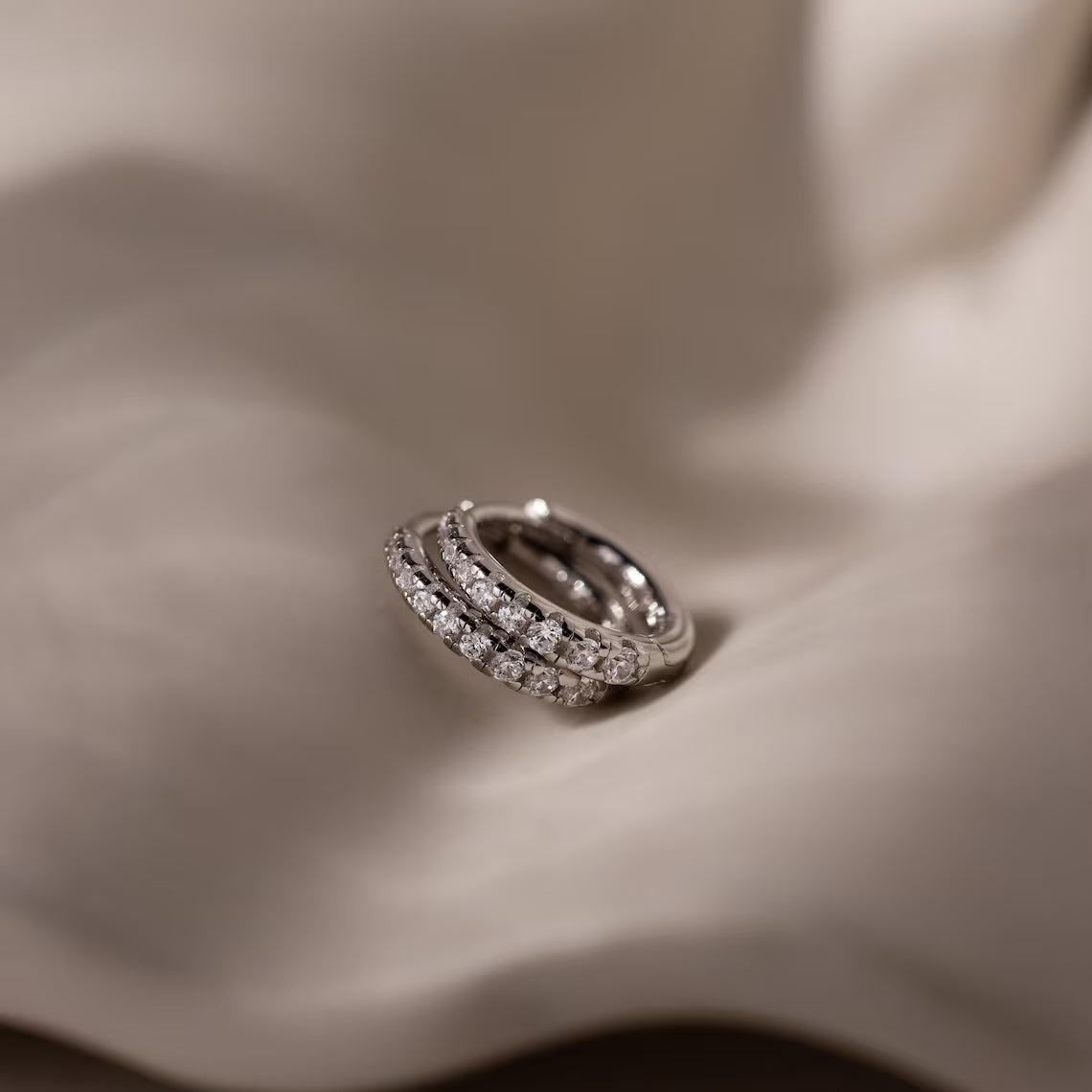 Silver hoop earrings with embedded diamond stones on a soft fabric background