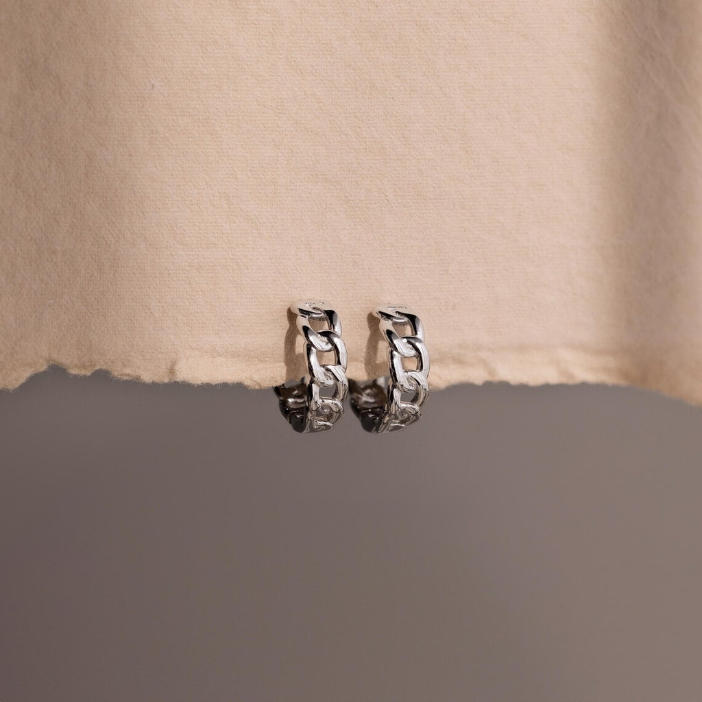 Pair of silver chain hoop earrings on a textured beige surface.