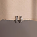 Pair of silver chain hoop earrings on a textured beige surface.