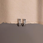 Pair of silver chain hoop earrings on a textured beige surface.