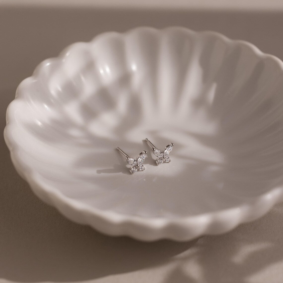 Pair of silver butterfly-shaped earrings on a textured white dish.