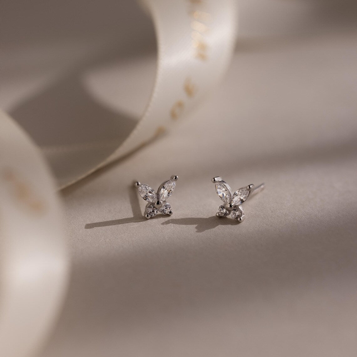 Pair of diamond silver butterfly earrings on a soft beige background