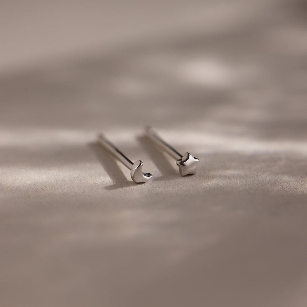 Pair of tiny silver moon and star earrings on a beige fabric background