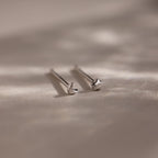 Pair of tiny silver moon and star earrings on a beige fabric background