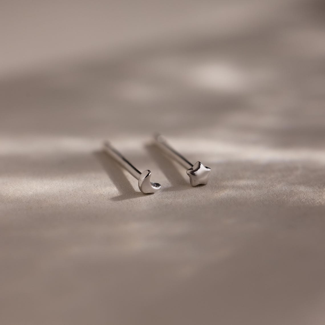 Pair of tiny silver moon and star earrings on a beige fabric background