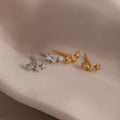 Two pairs of star-shaped earrings in gold and silver on a neutral background