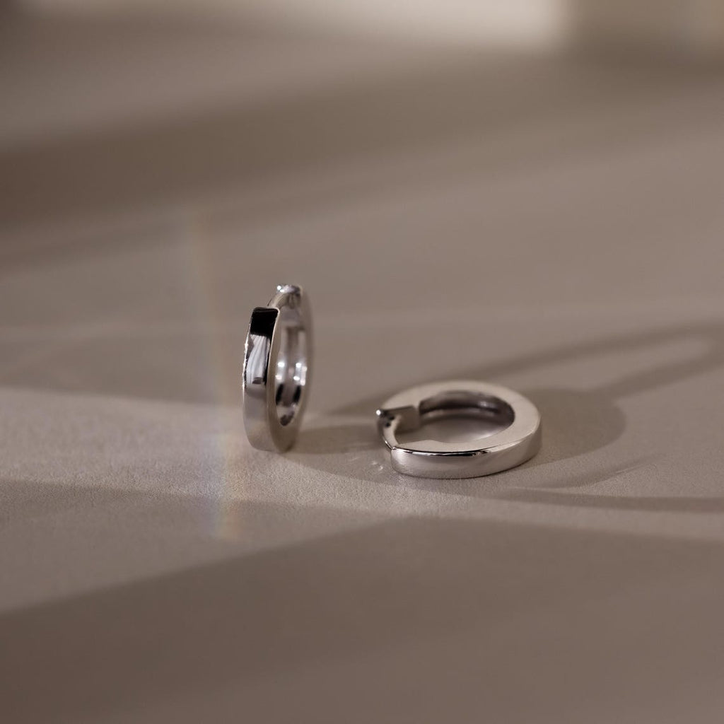 Pair of silver hoop earrings on a beige surface
