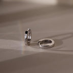 Pair of silver hoop earrings on a beige surface