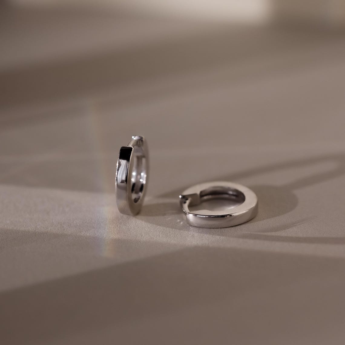 Pair of silver hoop earrings on a beige surface