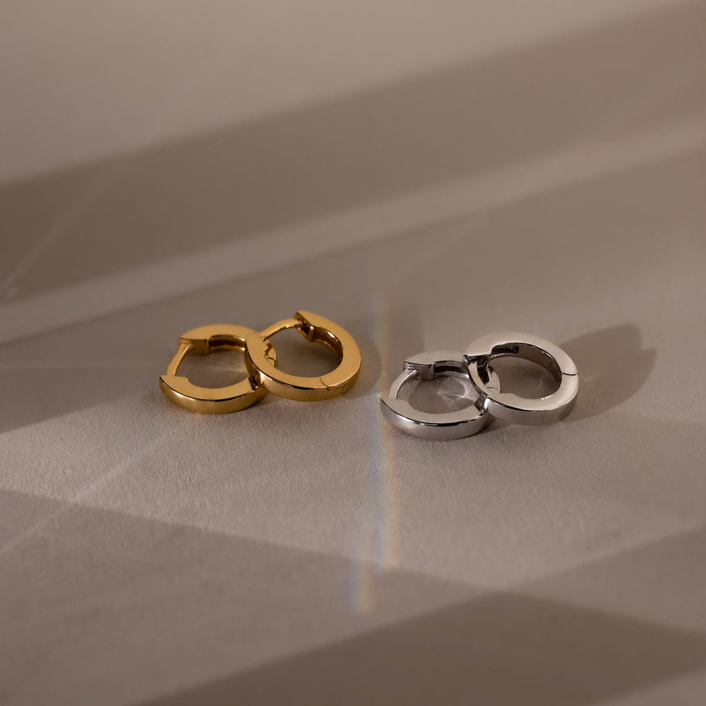 Two pairs of hoop earrings, one gold and one silver, on a neutral background.