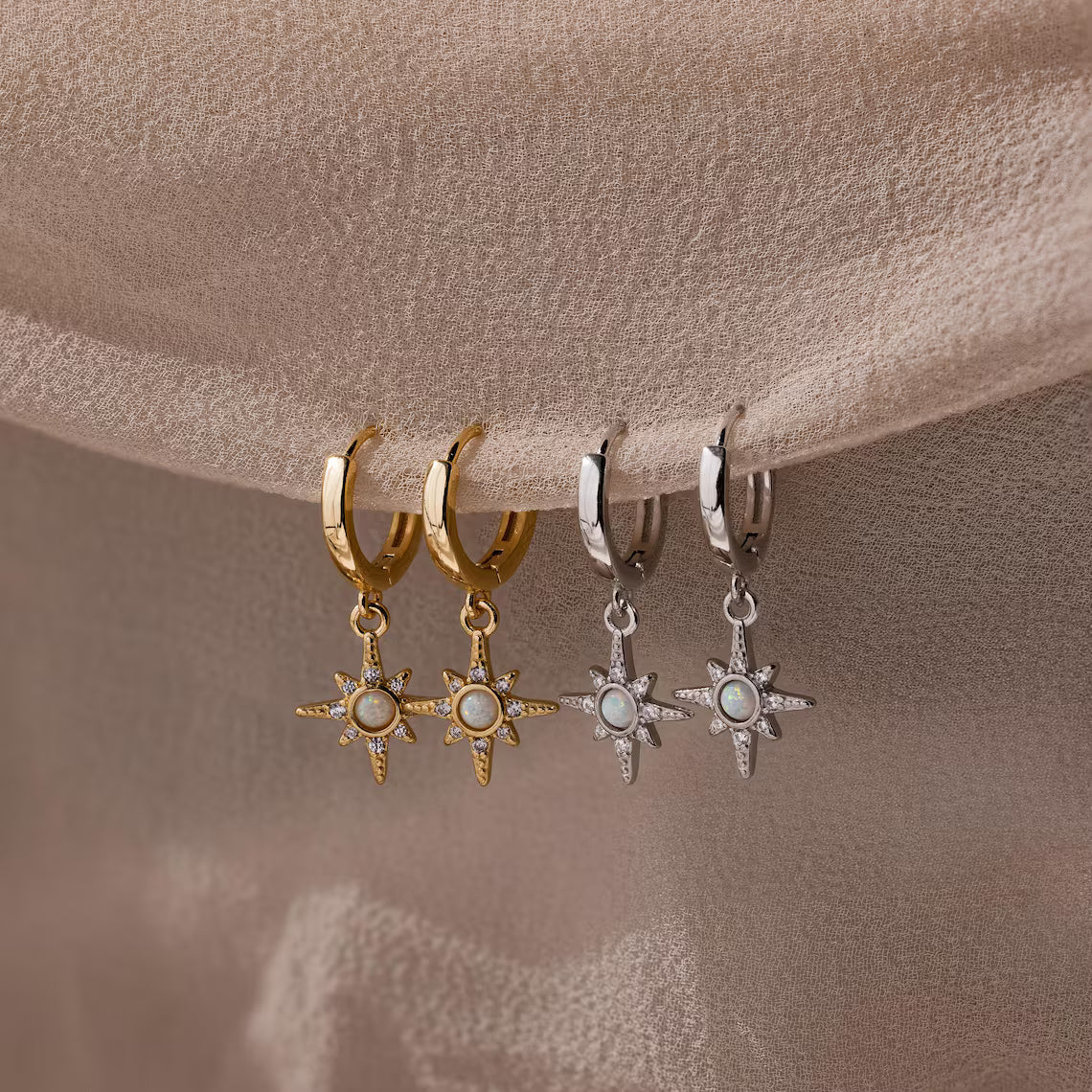 Two pairs of star-shaped earrings on gold and silver hoops against a beige background