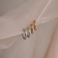 Four diamond hoop earrings in gold and silver on a soft fabric background