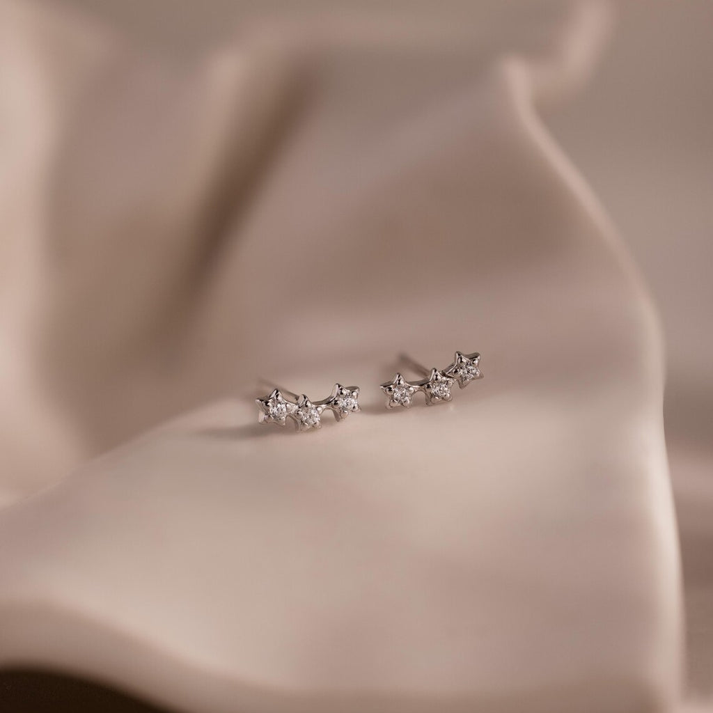 Pair of silver star stud earrings with clear stones on a beige fabric background