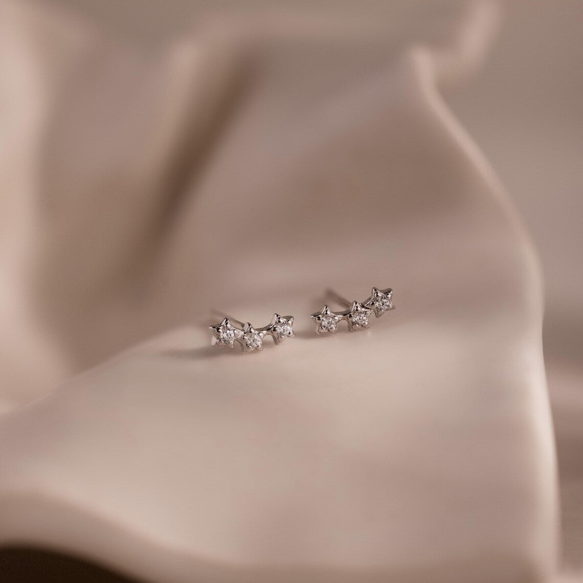 Pair of silver star stud earrings with clear stones on a beige fabric background