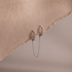 Silver pave hoop earrings with chain detail on a textured beige surface
