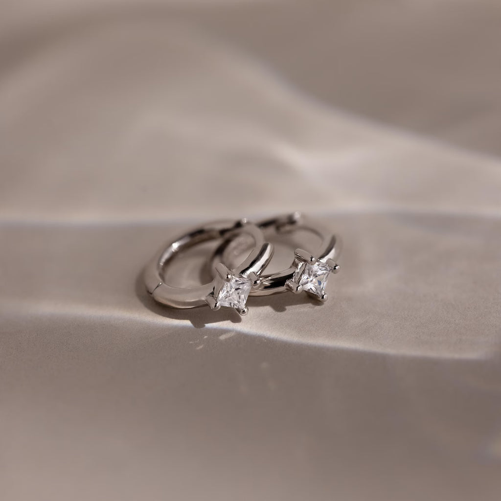 Silver huggie earrings with two diamond stones on a beige background