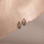 Pair of silver clear gemstone hoop earrings on a beige fabric background