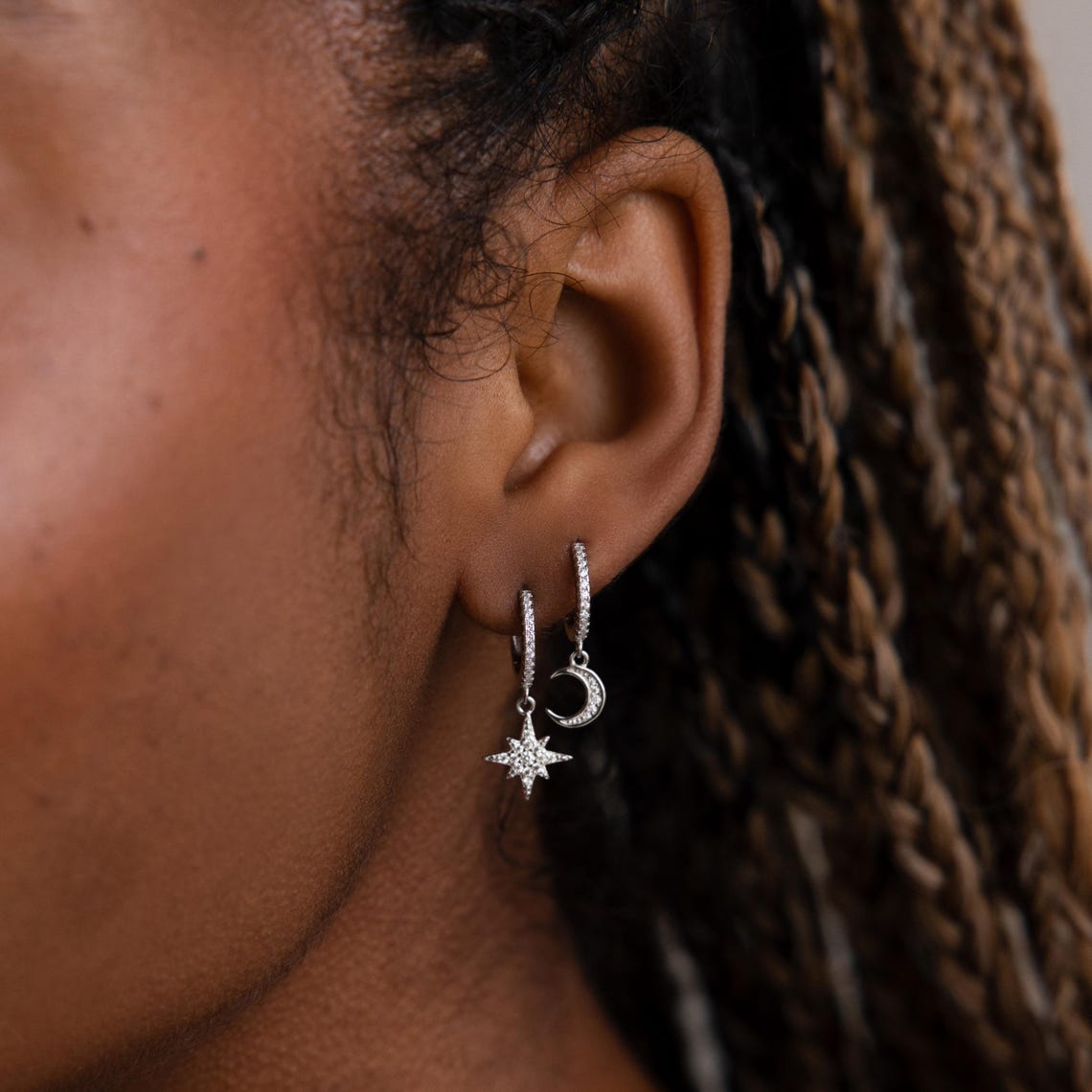 Close-up of an model wearing silver hoop earrings with star and moon designs.